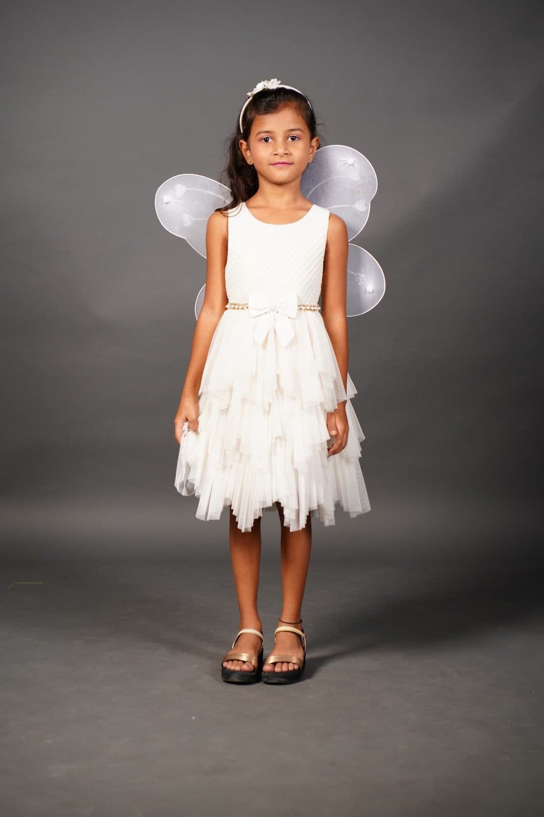Chaithrika in a white tulle dress with fairy wings against a grey studio backdrop