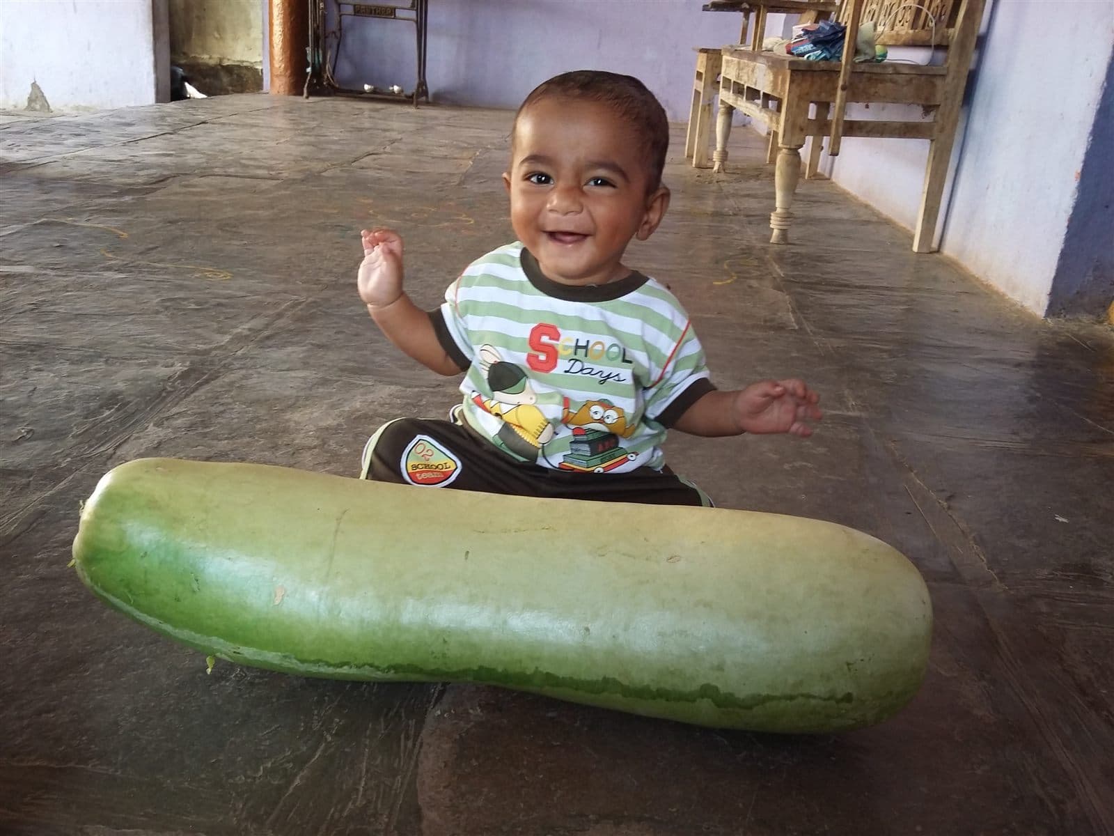 Baby Nihan in a striped tee sitting beside a giant bottle gourd