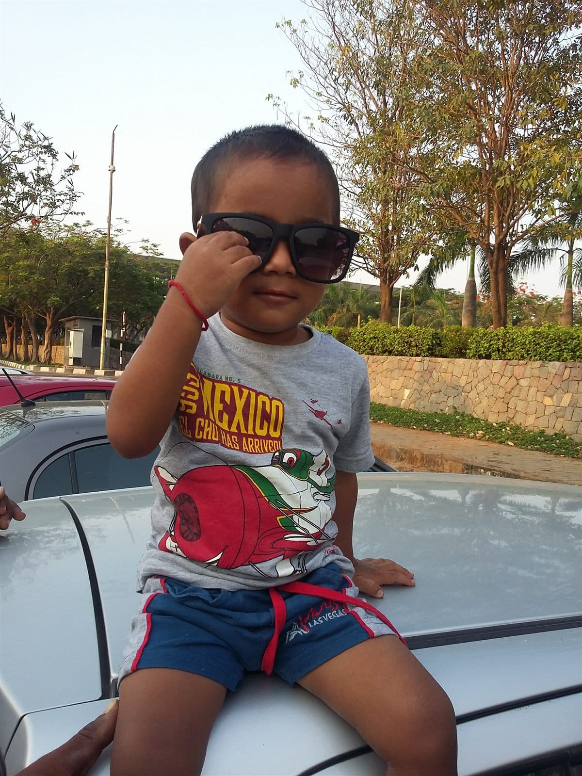 Toddler in sunglasses sitting on a car bonnet