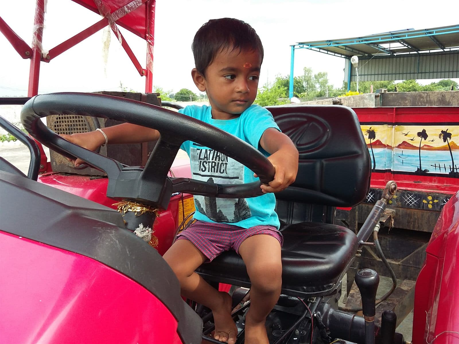 Toddler Nihan at the steering wheel of a big red tractor