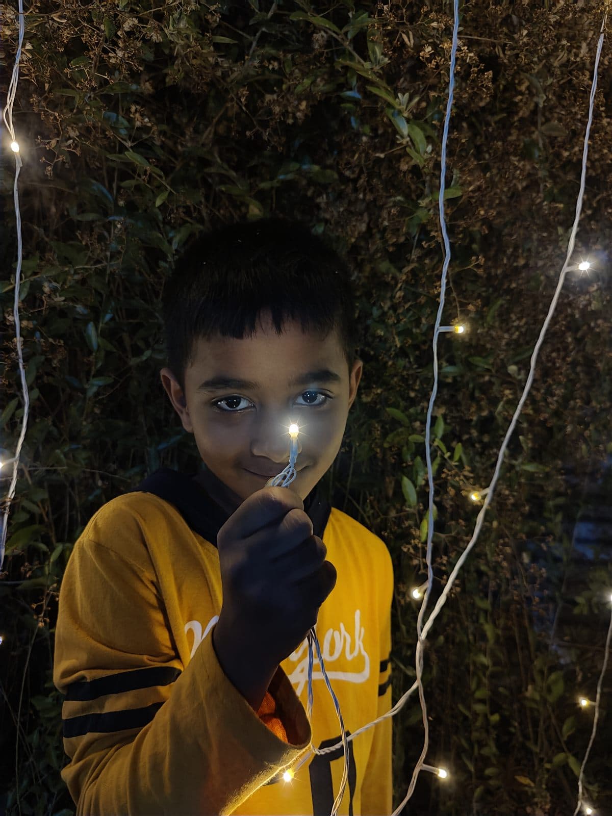 At night among fairy lights in a yellow hoodie, holding a small light